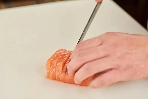 Chef hand slicing salmon close up.