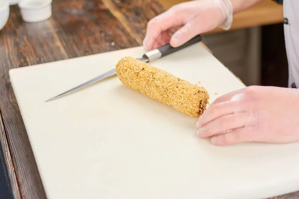 Chef hands with knife and long sushi roll.