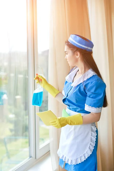 Jonge huishoudster schoonmaken van een venster. — Stockfoto