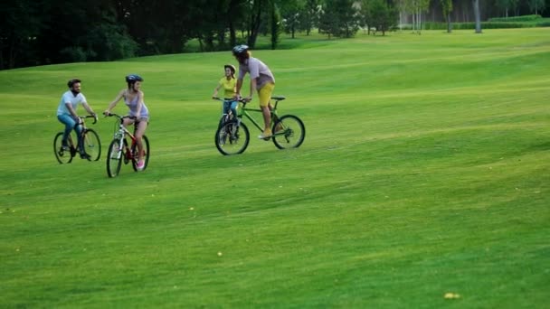 Quatre étudiants joyeux à vélo sur la pelouse verte . — Video
