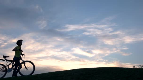Unga cyklister gå på kullen vid solnedgången. — Stockvideo