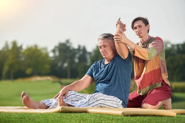 Terapeuta di yoga facendo massaggio tradizionale braccio thai ad un uomo anziano . — Foto Stock