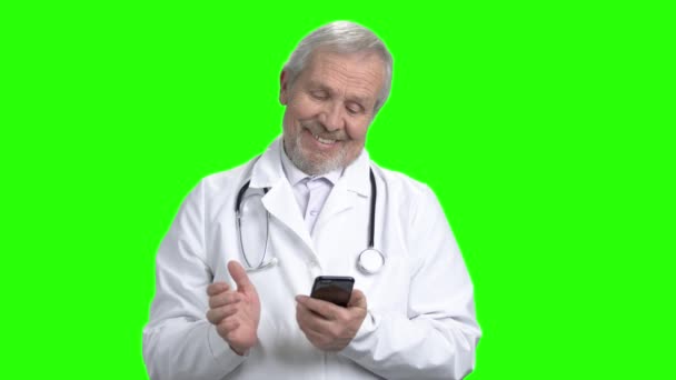 Alter lächelnder Arzt plaudert auf Smartphone. — Stockvideo