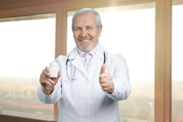 Viejo médico sonriente con lata de pastillas y como signo . — Foto de Stock