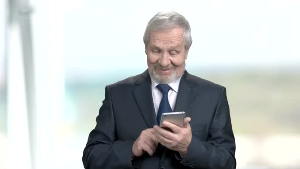 Äldre affärsman med smartphone, suddig bakgrund. — Stockvideo