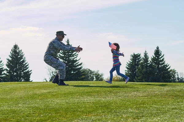 Girl running to her military father, side view.