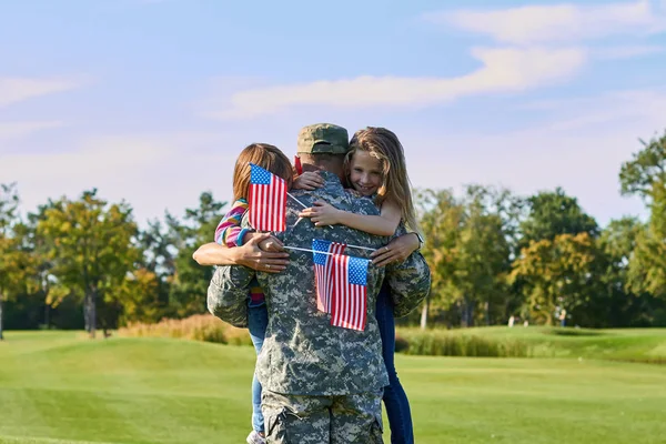 Soldado de vista trasera está abrazando a su familia con banderas de EE.UU. . — Foto de Stock