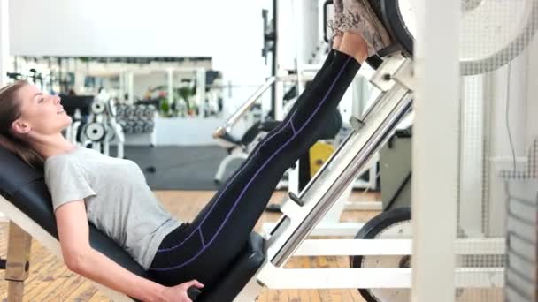 Vrouw met behulp van gewicht machine voor benen op sportschool. — Stockvideo