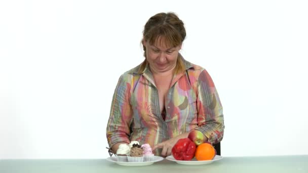 Mujer regordeta haciendo una elección entre pasteles y frutas . — Vídeo de stock