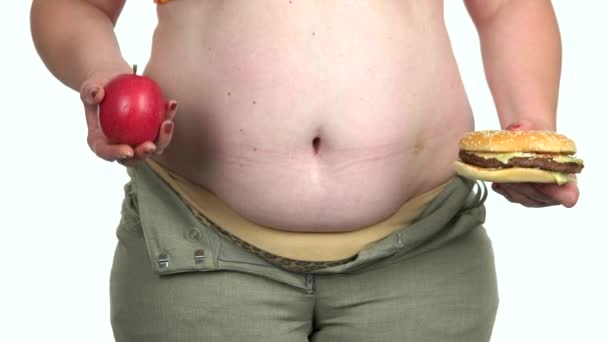 Толстая женщина выбирает между яблоком и бургером . — стоковое видео