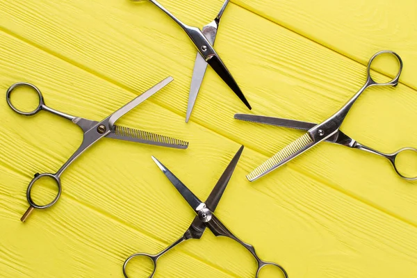 Hairdressing scissors on yellow wooden background.