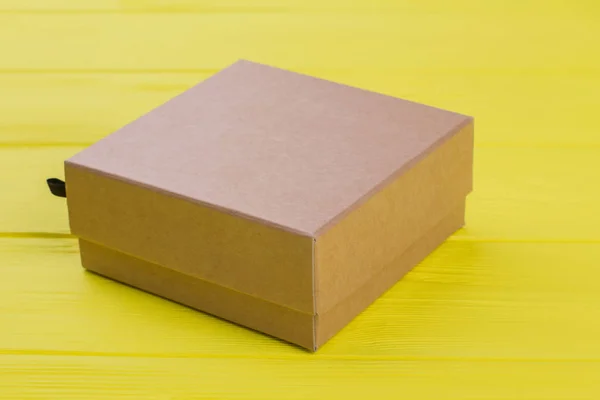 Kartonnen doos op gele houten ondergrond. — Stockfoto