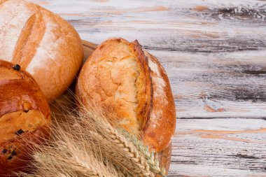 Ahşap zemin üzerinde kabuklu ekmek ve buğday kulakları.