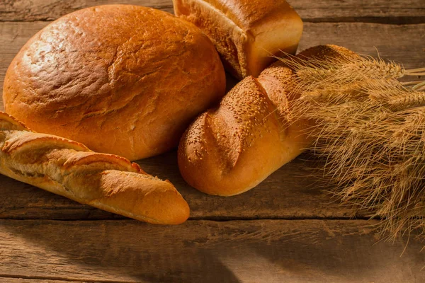 Brotlaibe und Weizenähren auf Holztisch. — Stockfoto