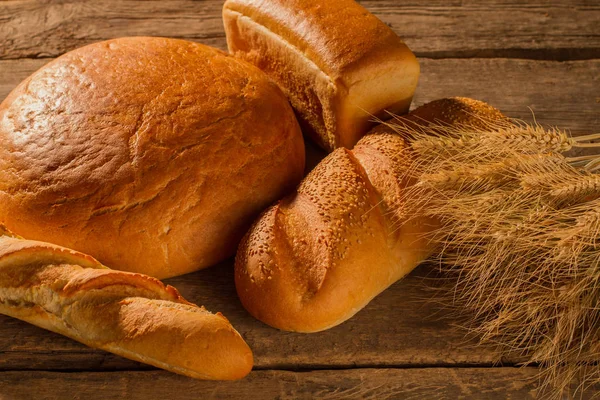 Φρέσκο ψωμί και αυτιά σιταριού σε ξύλινο φόντο. — Φωτογραφία Αρχείου