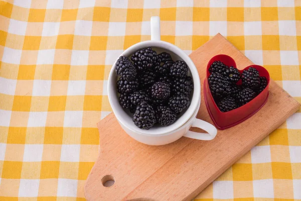 Cup and heart-shaped form are filled with blackberries. — Stock Photo, Image