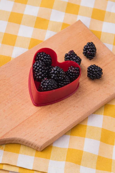 Red plastic heart-shaped form with blackberries. — Stock Photo, Image