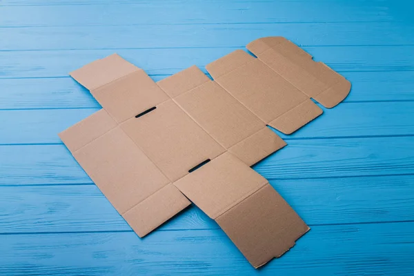 Caja de cartón beige onfolded en una madera azul . —  Fotos de Stock