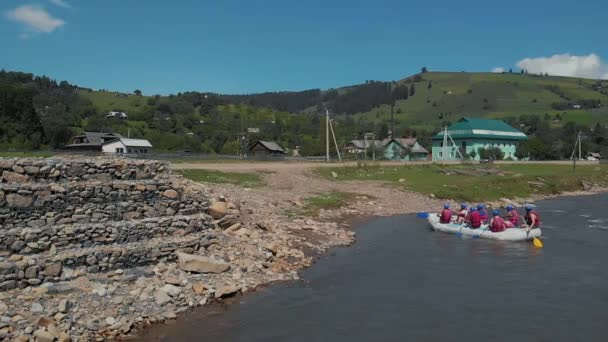 Emberek egy csoportja kajakban a folyón a part menti falu közelében. — Stock videók