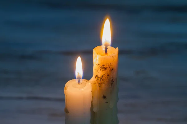 Two glowing candles with melted wax.