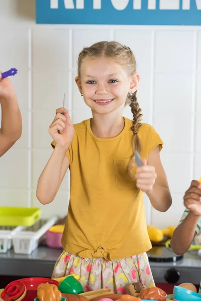 Glücklich lächelndes Mädchen blickt in Spielzeugküche in die Kamera. — Stockfoto