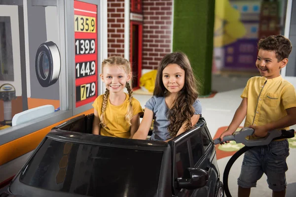 Little girls sitting in car at gas station in playroom. — ストック写真