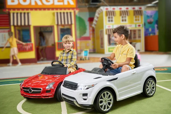 Two preschool boys ride on toy car in playground. — ストック写真