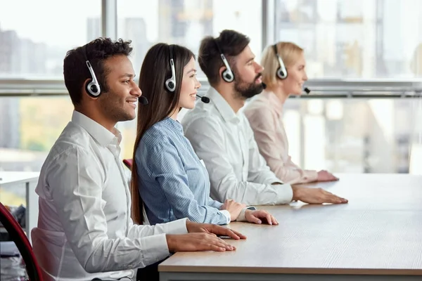 Equipo de operadores de call center sentados con las manos en la mesa . — Foto de Stock