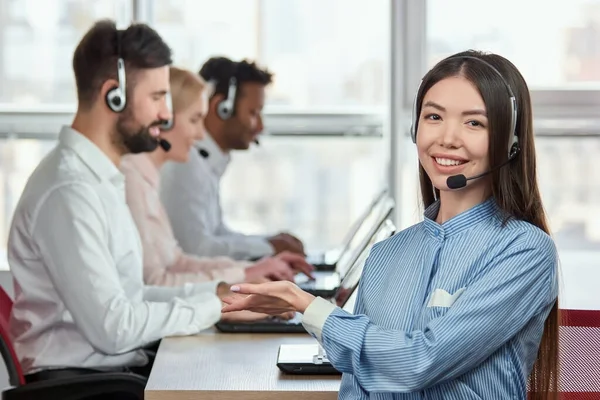 Joven operadora apuntando de la mano a sus compañeros de trabajo . — Foto de Stock