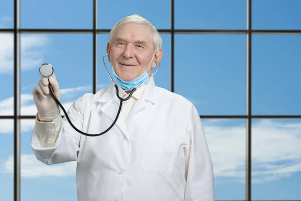 Senior läkare som håller stetoskop mot fönster backgorund. — Stockfoto