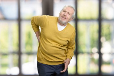 Portrait of unhealthy old senior man with bottom back pain.