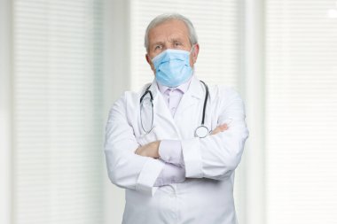 Serious doctor with medical mask and crossed arms.