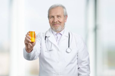 Old senior doctor giving orange can of pills to you.