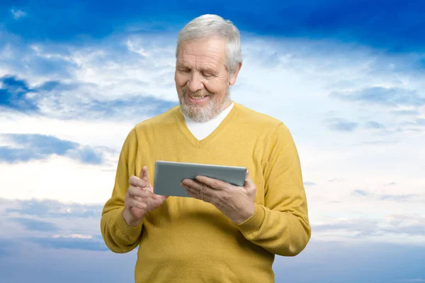 Old man with tablet over blue sky background.