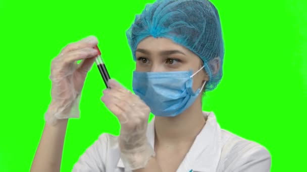 Young female doctor with mask looks at blood test tube. — Stockvideo