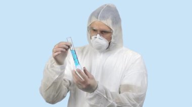 Antiviral koruyucu giysili bir tıp çalışanı elinde mavi sıvıyla test tüpü tutuyor..