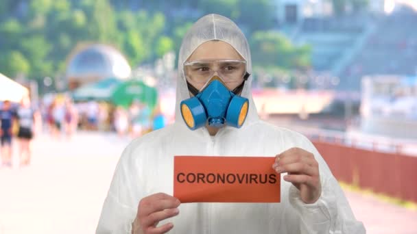 Mann mit Atemmaske und Schutzanzug mahnt zur Vorsicht vor Coronavirus. — Stockvideo