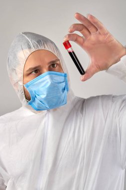 Maskeli doktor parmaklarında kan testi tüpü tutuyor..