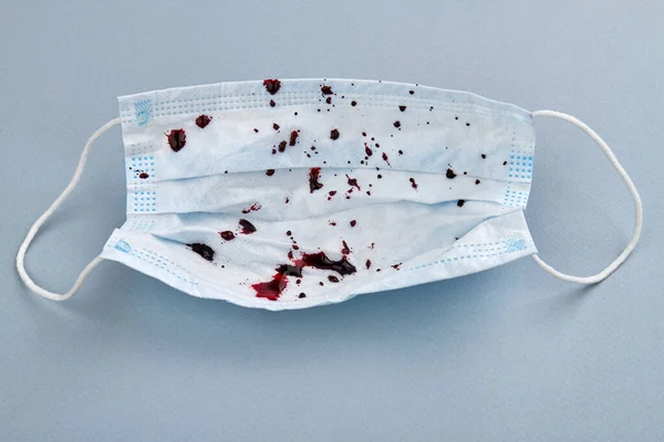 Medical protective mask with blood drops on grey background.