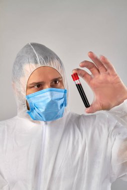 Koruyucu elbiseli bir adam elinde kan testi tüpü tutuyor..