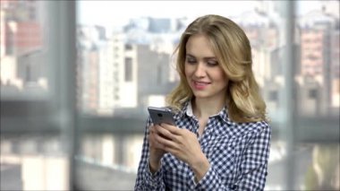 Ofisteki neşeli genç kadın telefonla mesaj atıyor..