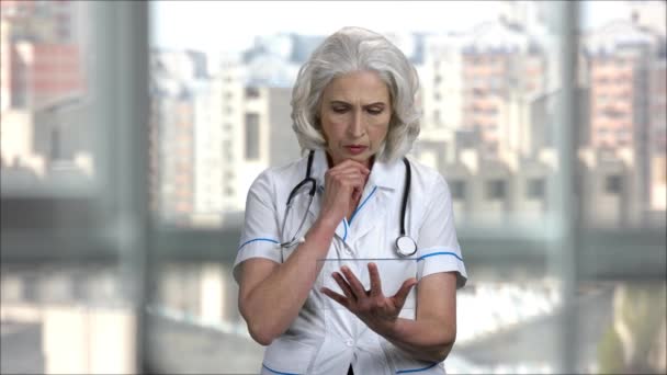 Viejo médico femenino severo con la tableta copyspace de vidrio transparente en blanco . — Vídeo de stock