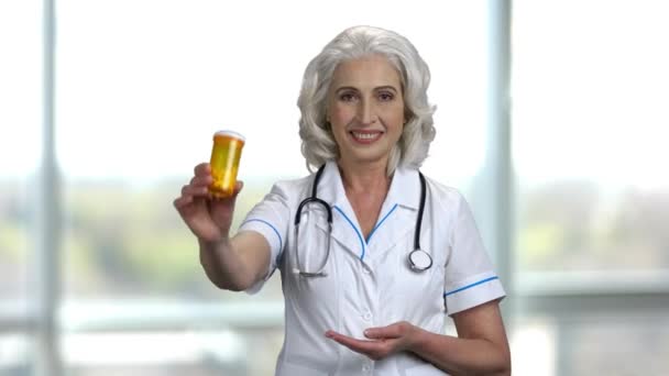 Old cheerful female doctor advertising yellow bottle of medicine. — Stock Video