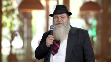 Yaşlı sakallı adam mikrofonla konuşuyor..