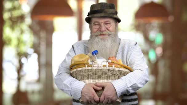 Porträt eines alten Rentners, der einen Korb mit Lebensmitteln hält. — Stockvideo