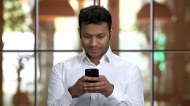 Kahverengi tenli Hintli iş adamı akıllı telefonunu kullanarak mesaj atıyor..