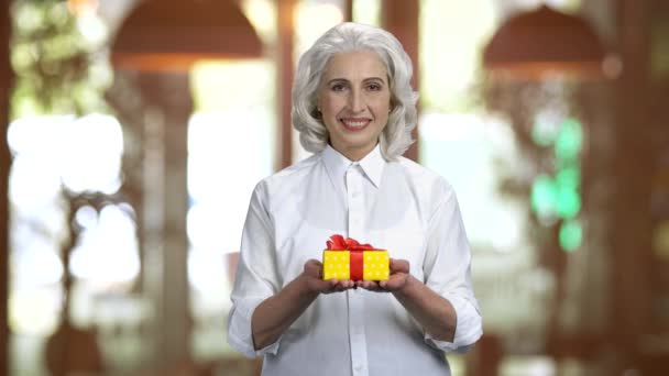 Vieille dame portant une chemise blanche montrant boîte cadeau dans les deux mains . — Video