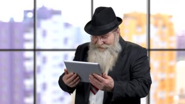 Takım elbiseli yaşlı işadamı tabletinde komik mimler izlerken gülüyor..