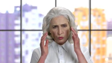 Baş ağrısı olan yaşlı kadın, şakaklarına masaj yapıyor..