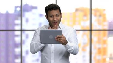 Resmi tişörtlü genç esmer adam iki eliyle tableti tutuyor..